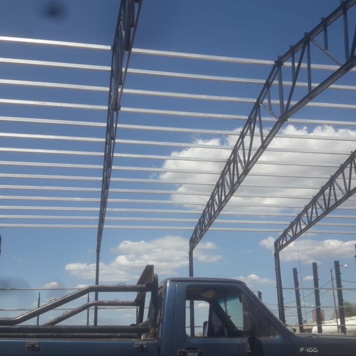 Camioneta azul con techo de metal contra un cielo brillante con nubes.