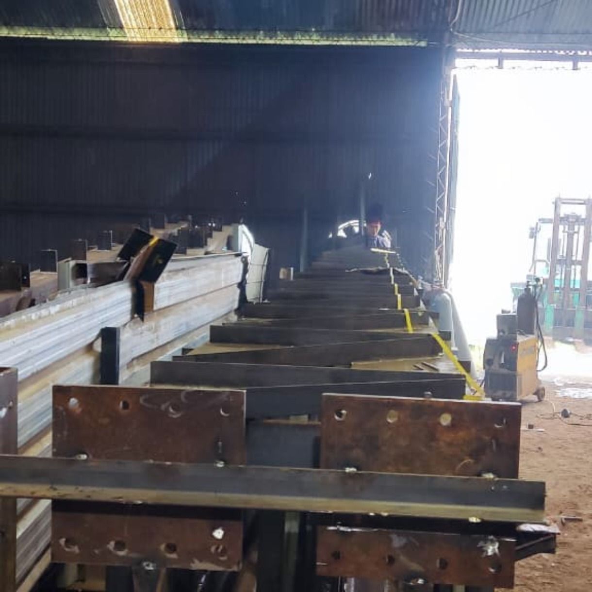 Vigas de acero apiladas en un almacén industrial junto a una puerta abierta y luminosa.