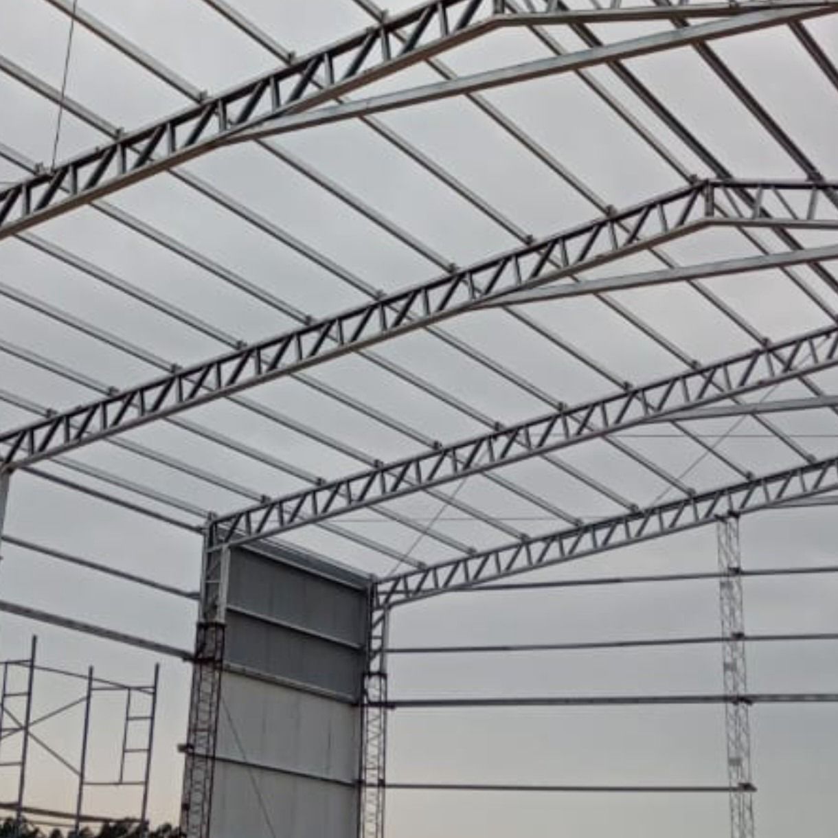 Interior de una gran estructura metálica de almacén con cerchas de techo arqueadas en construcción.