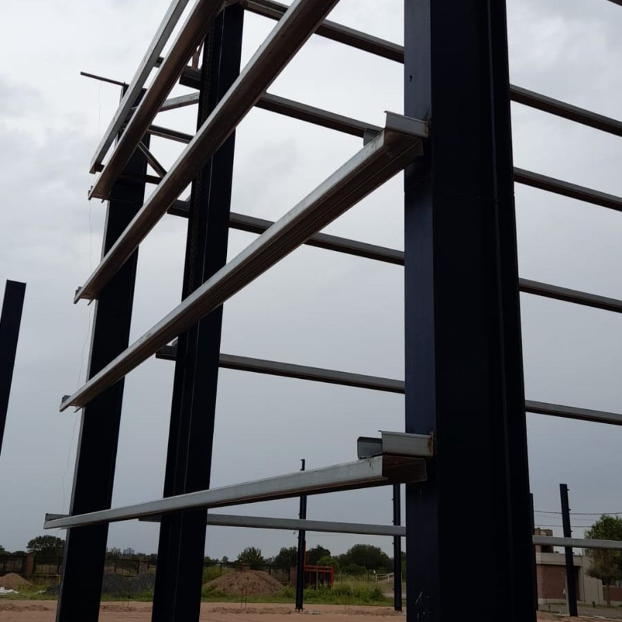 Estructura de acero en construcción en un día nublado, con columnas negras y vigas horizontales.
