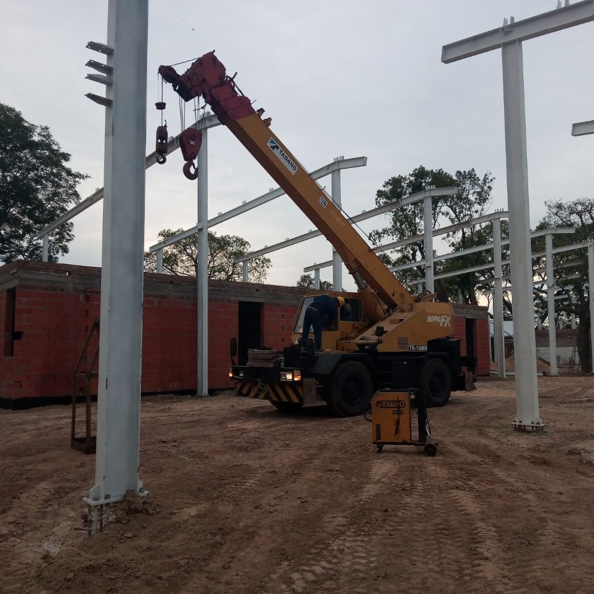 Un camión grúa amarillo levanta objetos cerca de postes de hormigón en una obra de construcción.