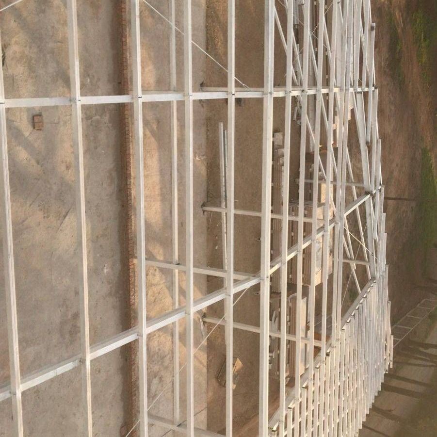 Puerta de metal blanco junto a un camino de tierra con una pequeña estructura de piedra al fondo, vista desde un ángulo.