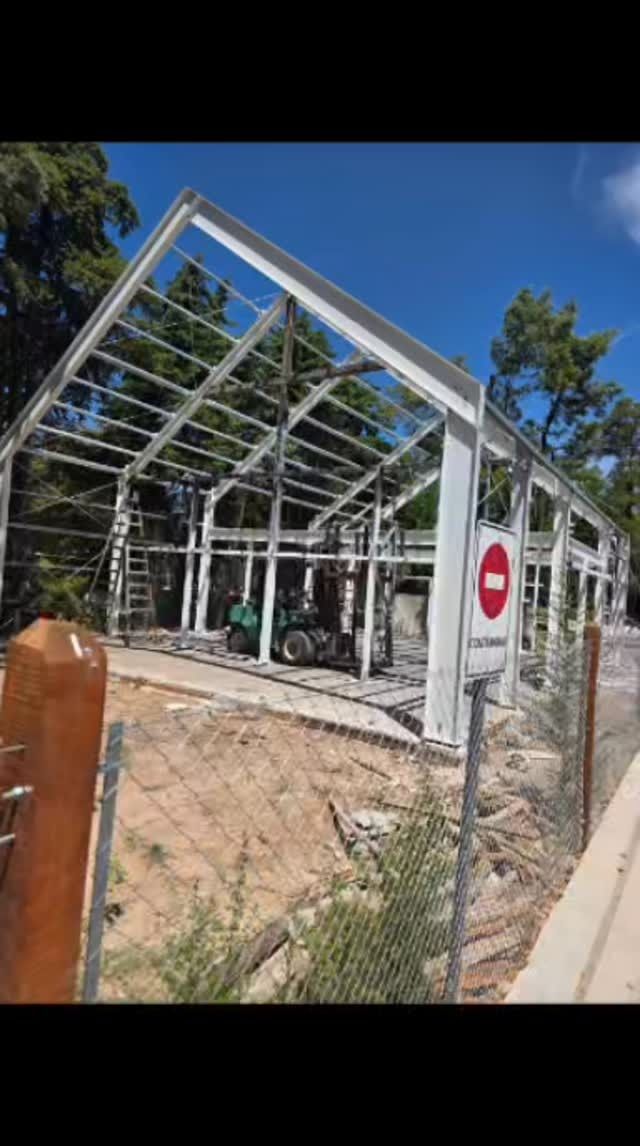 Estructura de vidrio y metal dañada detrás de una cerca de alambre con un panel de señal de alto.