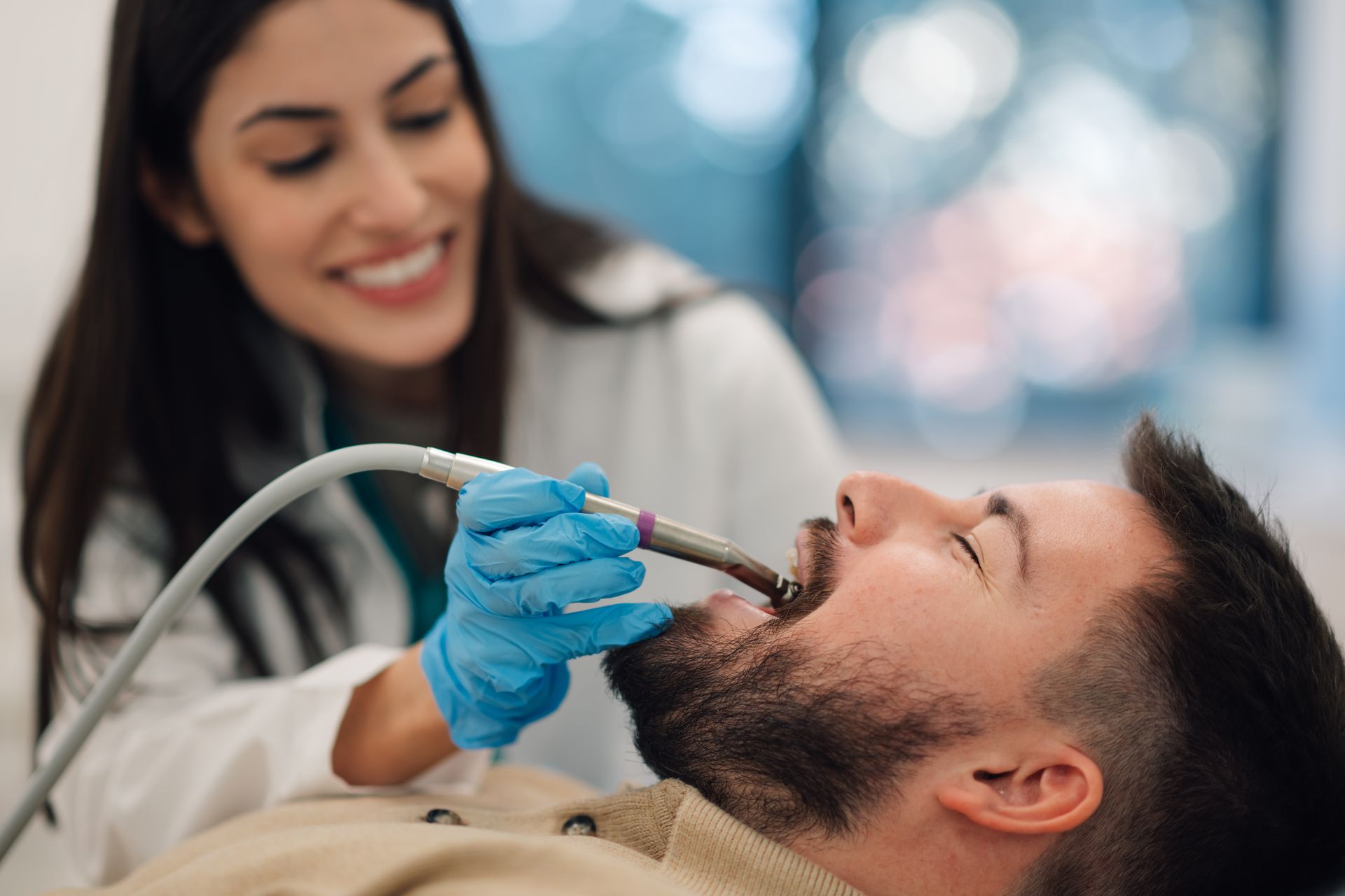 Dentist in blue gloves using a tool on a reclining patient during a dental exam
