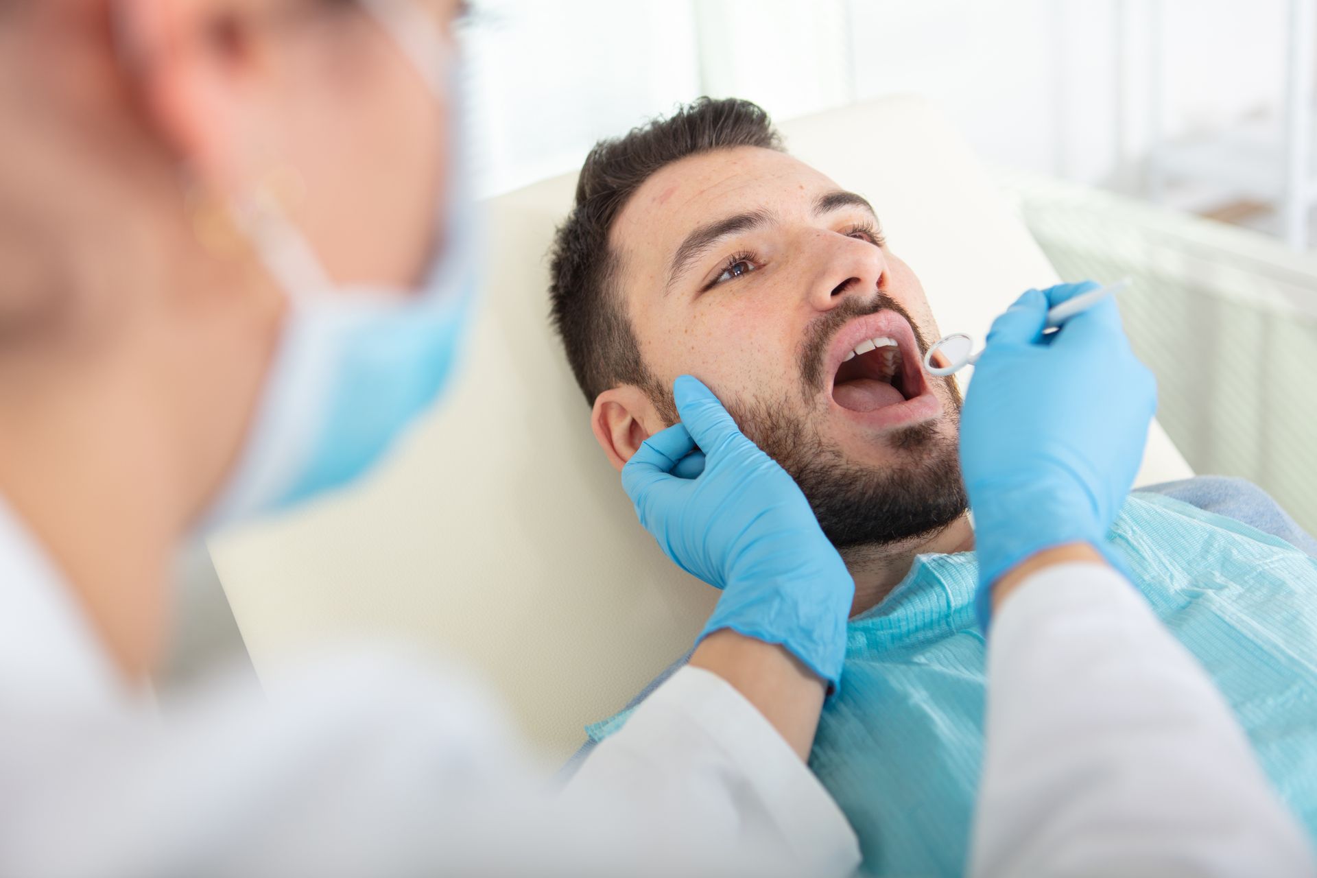 Dentist examining a patient’s open mouth in a bright clinic, wearing blue gloves and a mask