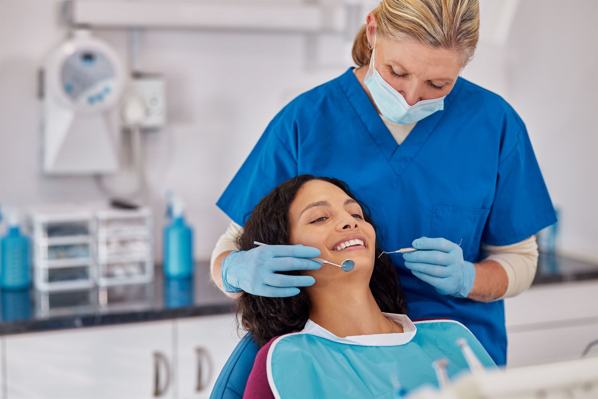 Dentist examining a patient in a dental clinic, both wearing blue scrubs and gloves