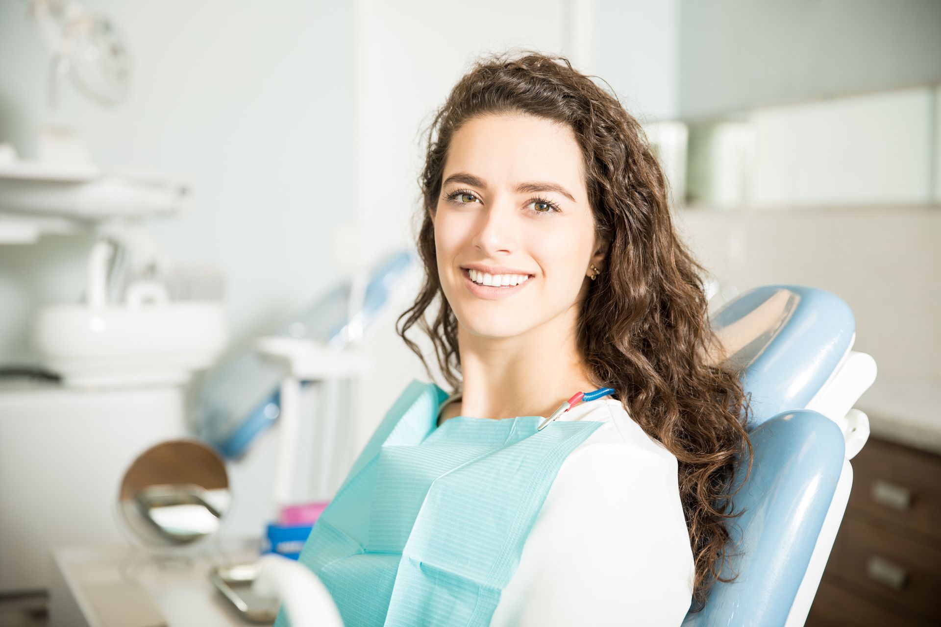 Smiling patient seated in a dental chair with a blue bib in a bright clinic
