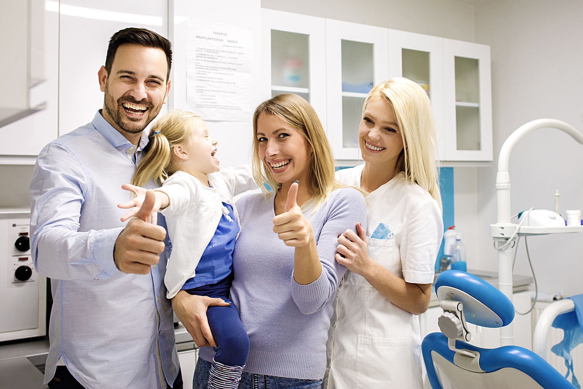 Smiling dental team and child in a bright clinic, all giving thumbs up.