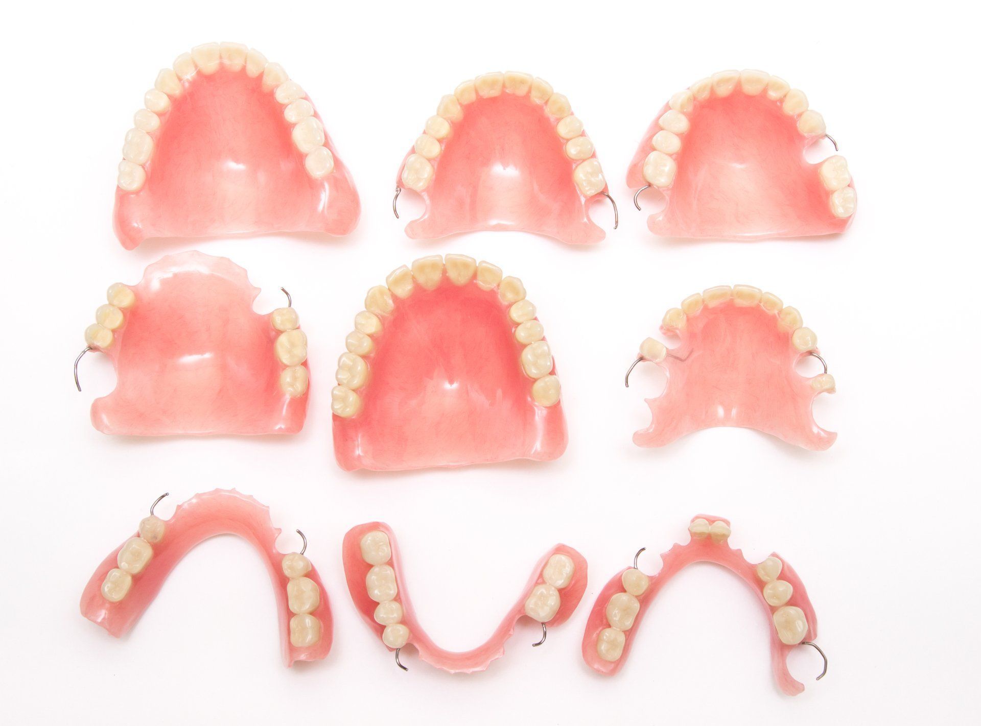 Assorted pink dentures and partial dental plates arranged on a white background