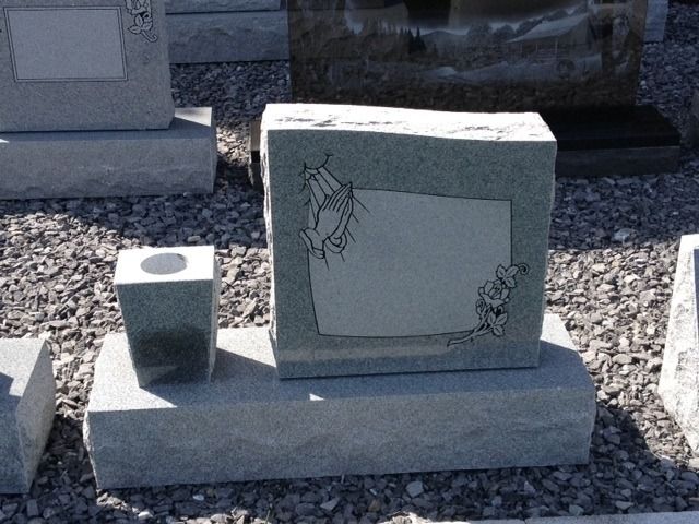 Gray granite memorial with an engraved plaque and a small candle holder on a gravel bed