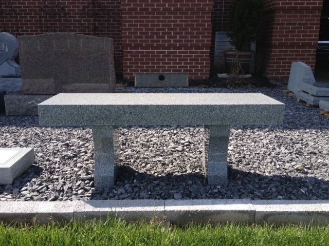 Outdoor stone bench on gravel in front of a brick building