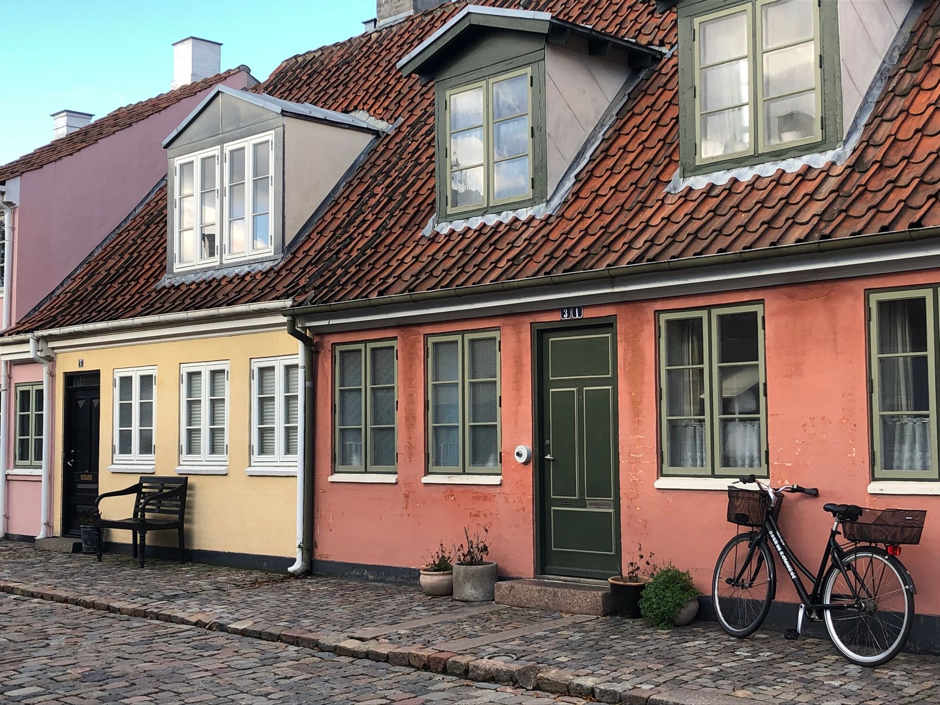 Colorful row of houses with red tile roofs on a cobblestone street, with a bicycle parked outside.