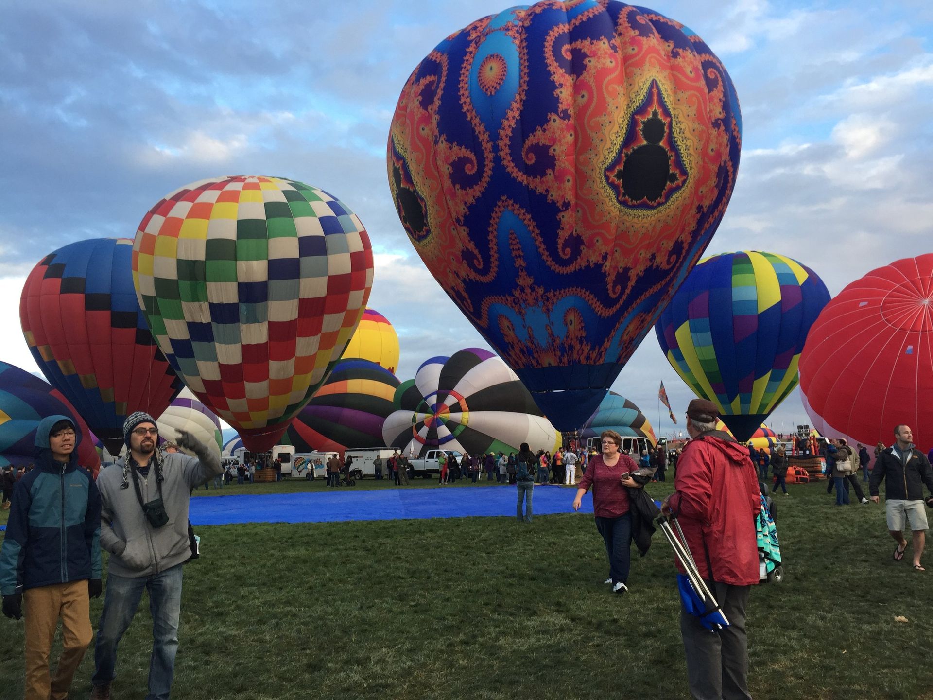 Hot air balloons inflation on a grassy field, including a large blue-and-orange balloon and people in jackets.