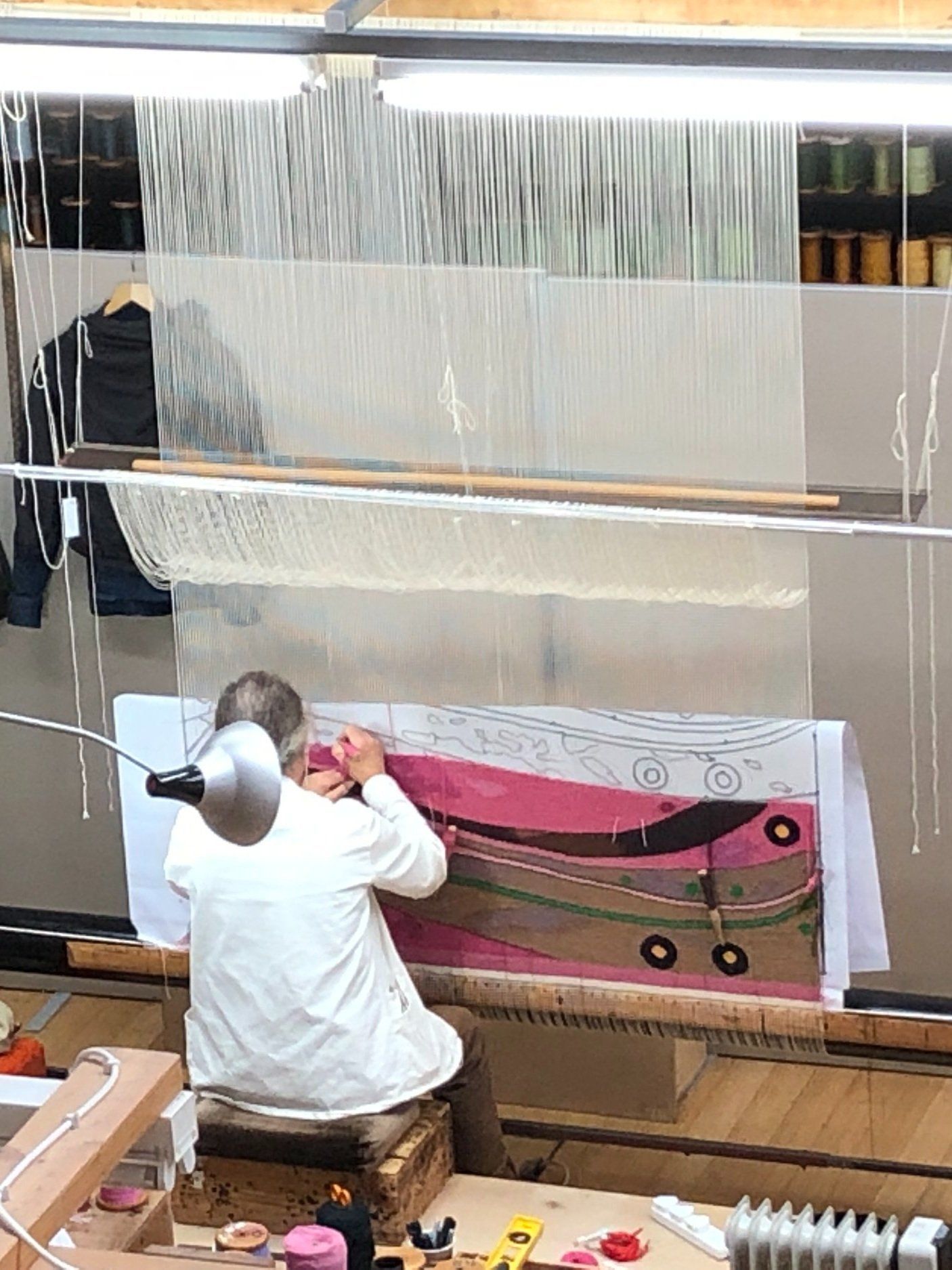 Person weaving a pink textile on a loom in a workshop