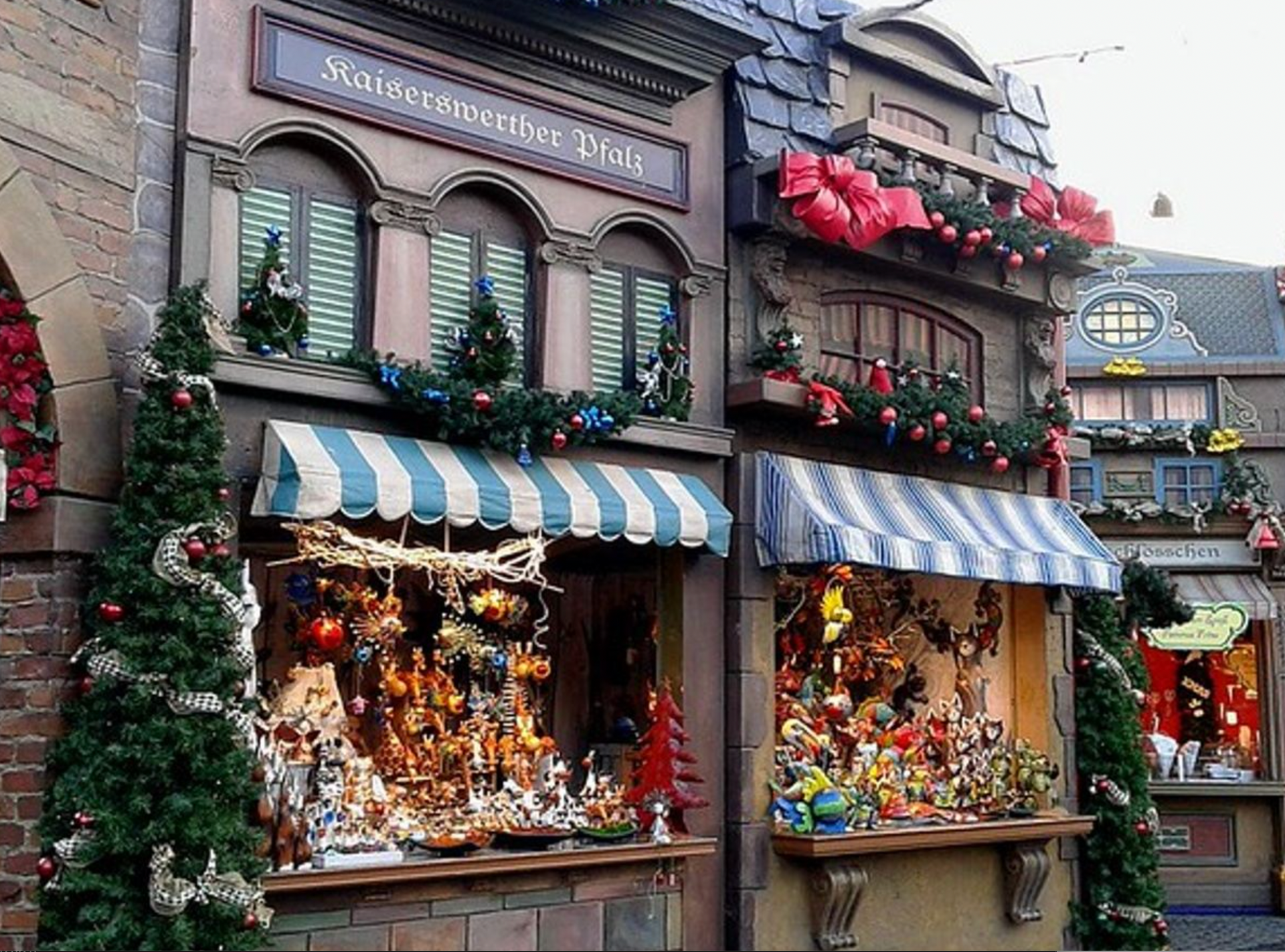 Festive holiday shopfront with striped awnings, decorated windows, and red flowers under the eaves