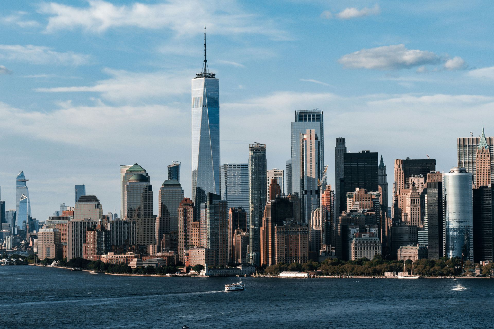 Manhattan skyline with One World Trade Center above the waterfront under a partly cloudy sky