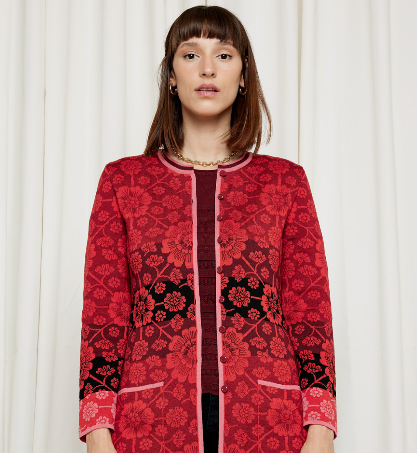 Woman wearing a red floral jacket against a light curtain backdrop