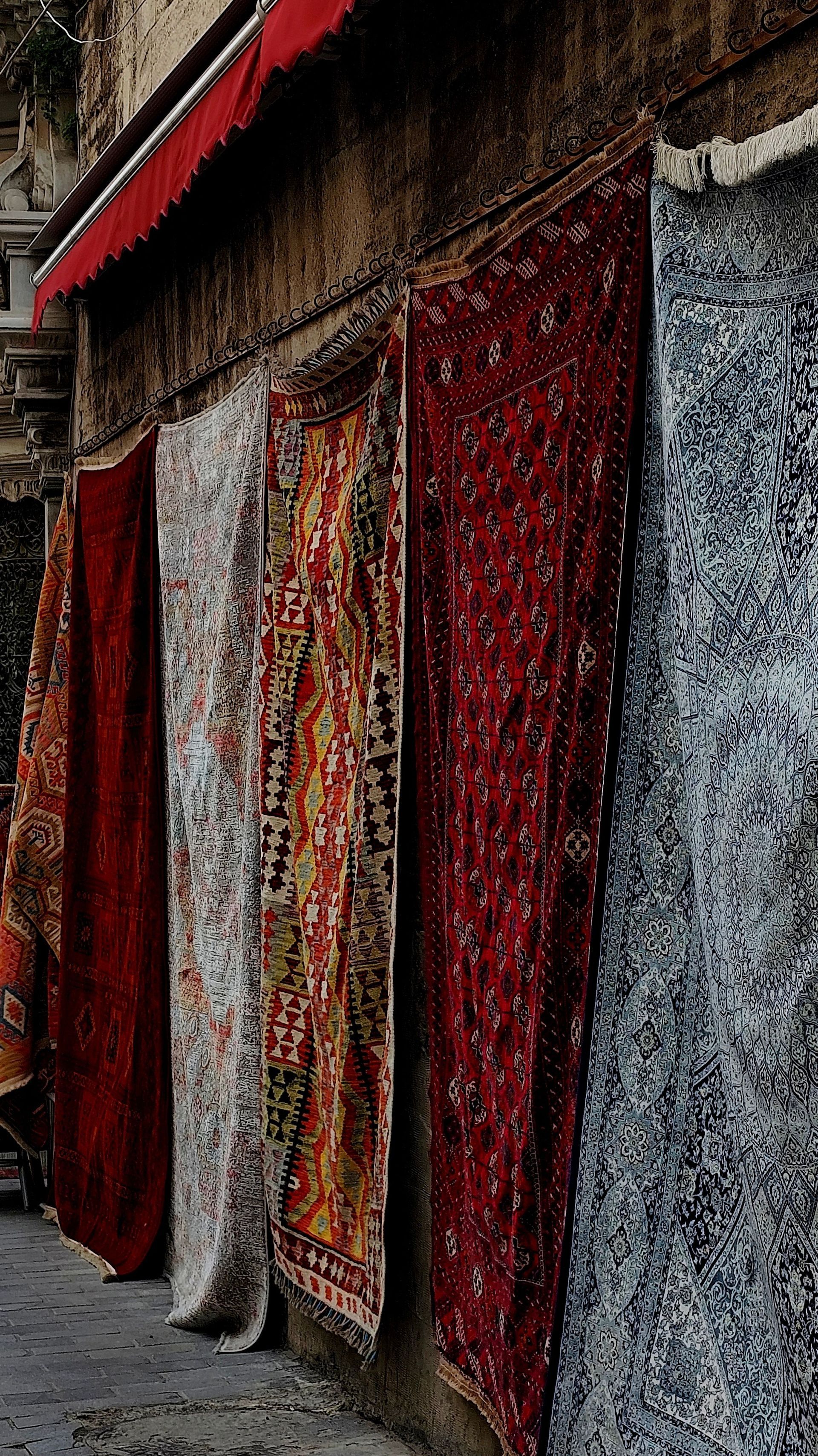 Shopfront with red and gray patterned curtains hanging over windows along a narrow street