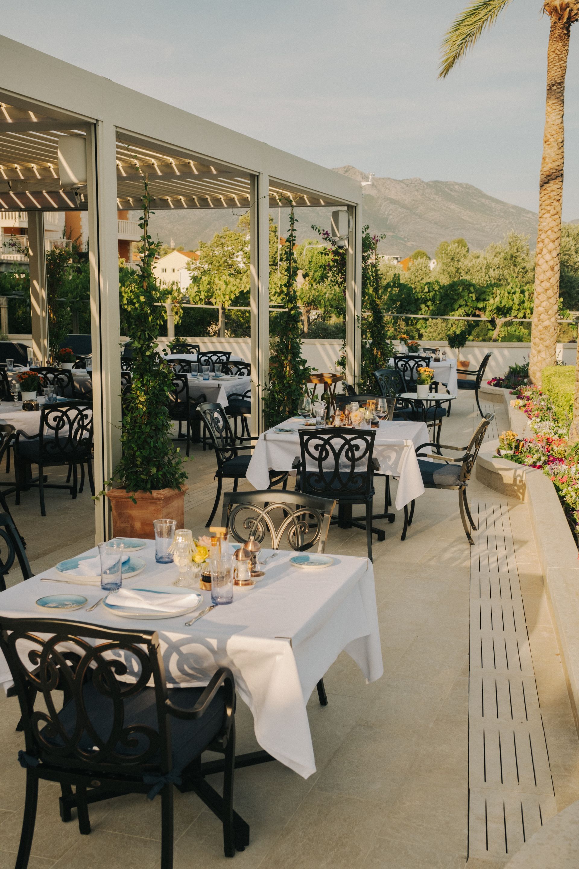 A restaurant with tables and chairs under a pergola with mountains in the background, Kapetanov Dvor