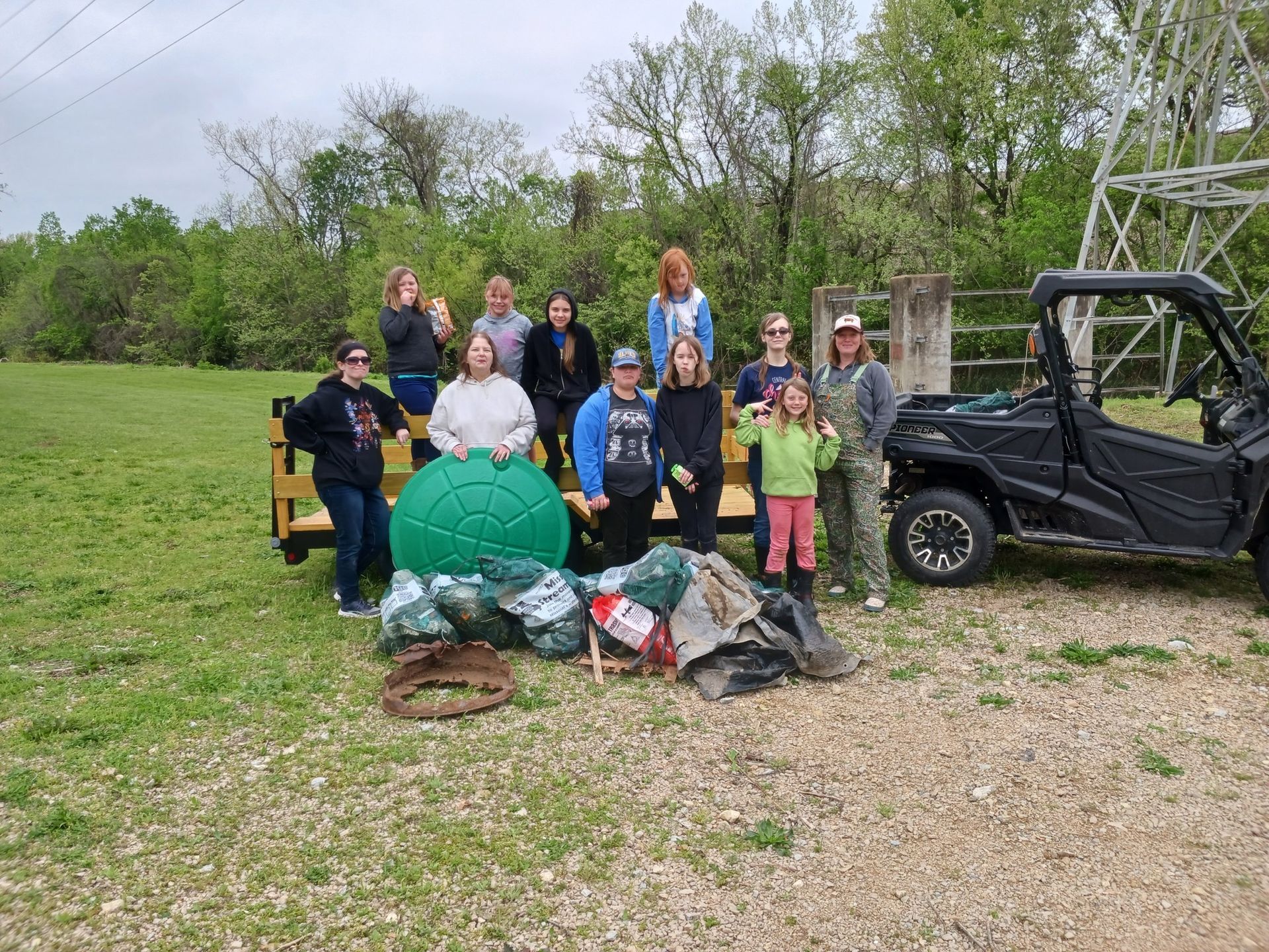 Group of people posing outdoors beside a large green sphere, trash bags, and an off-road vehicle.