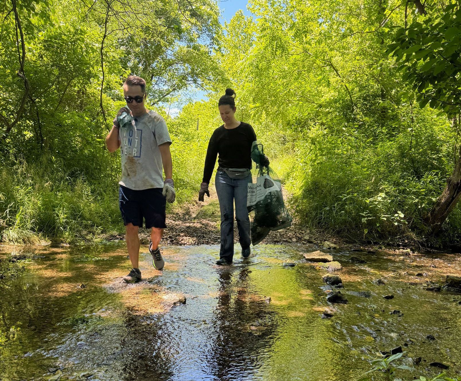 A man and a woman are walking through a stream in the woods.