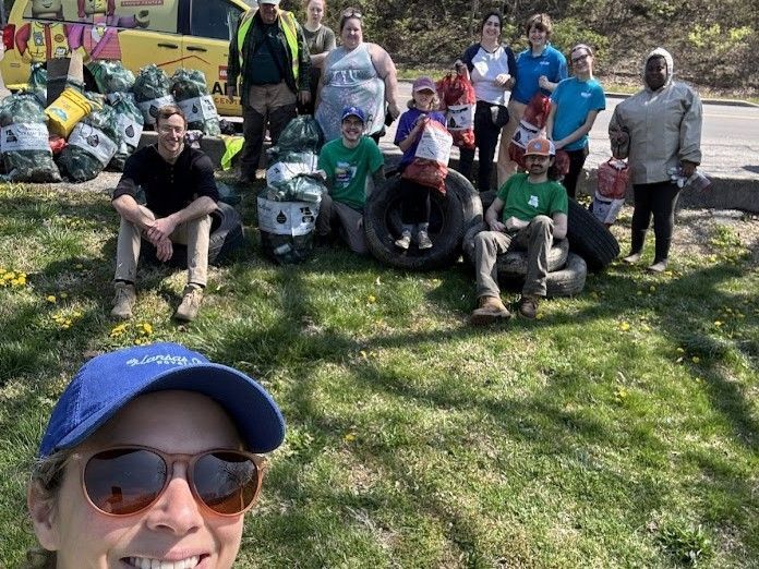 Group of people posing outdoors on grass, some seated on ATVs, with a smiling woman in sunglasses in the foreground
