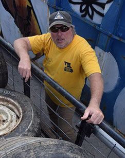 A man in a yellow shirt is leaning on a railing next to a tire.