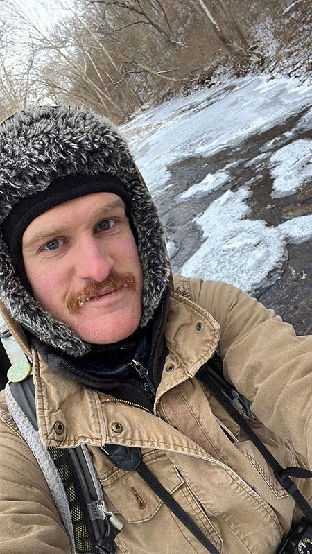 A man wearing a fur hat and a jacket is taking a selfie.