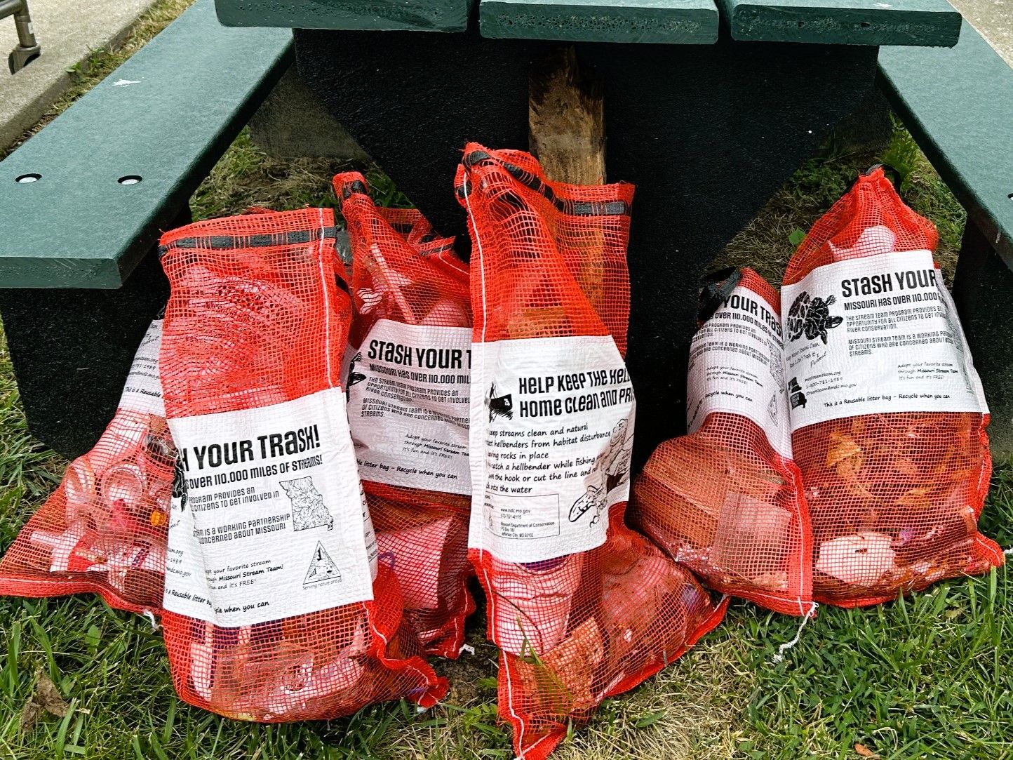 A bunch of bags of trash are sitting on top of a picnic table.
