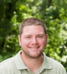 A man with a beard is smiling for the camera while wearing a green shirt.