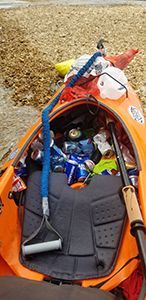 The inside of an orange kayak filled with cans , fishing rods , and a shovel.