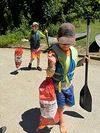 Two children carrying paddles and life jackets on a sunny path near the water
