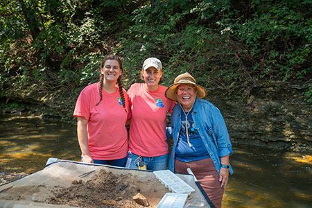 Three women are posing for a picture in front of a river.