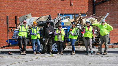 A group of people are standing in front of a trailer filled with trash.