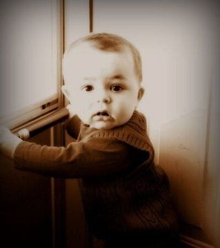 A baby is sitting in front of a window looking at the camera