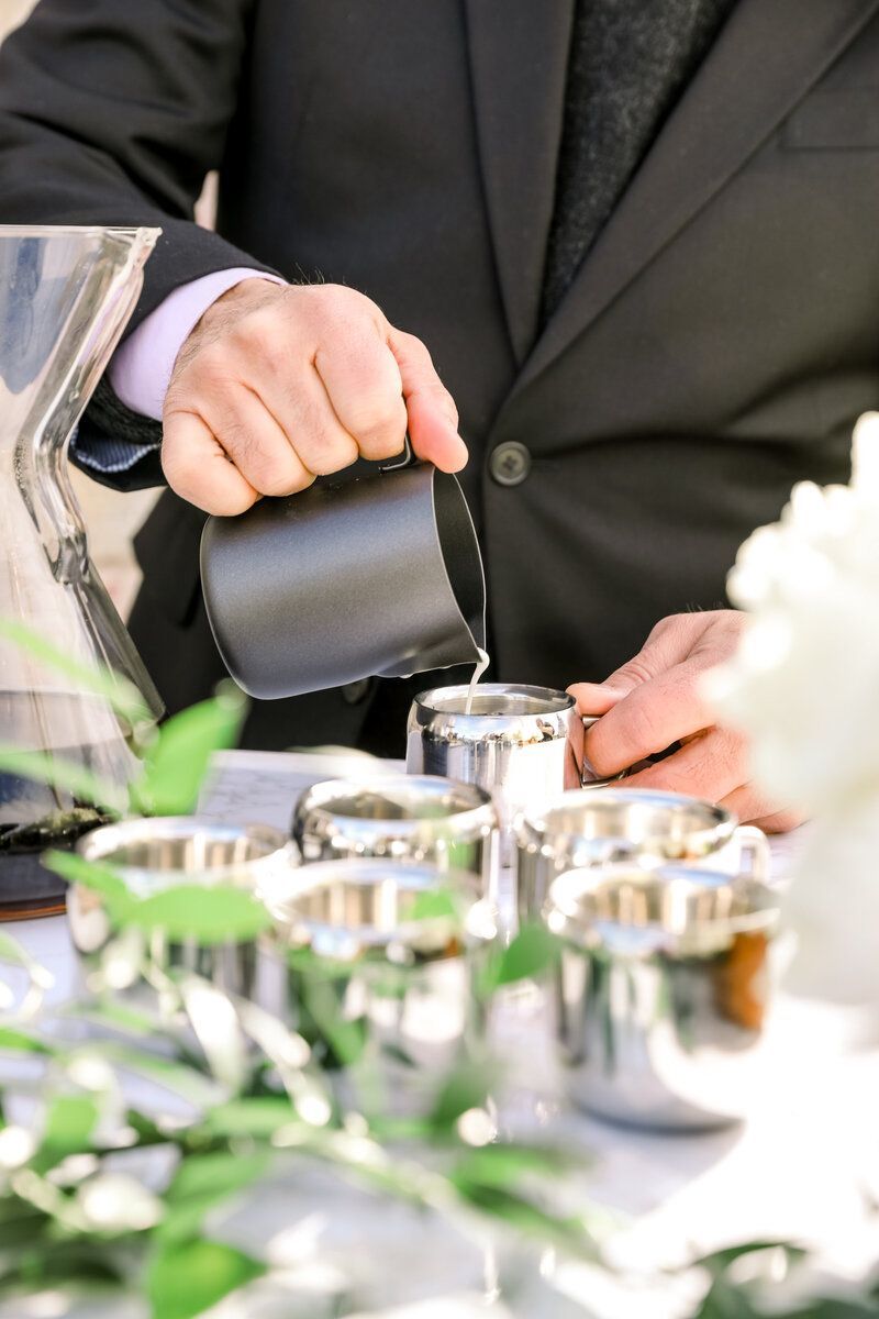 A man in a suit is pouring liquid into a cup.