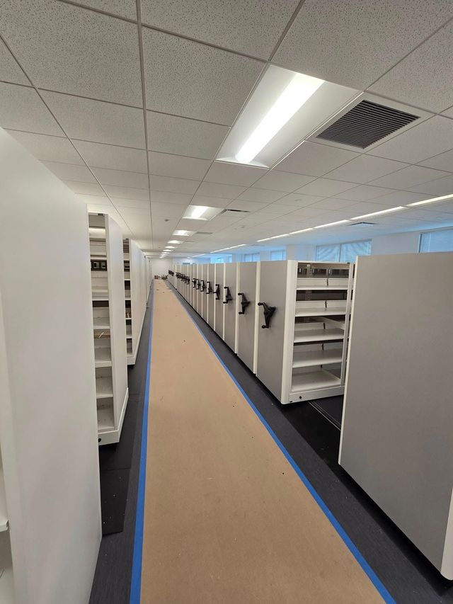 Office cubicle aisle with white partitions, blue carpet edging, and fluorescent ceiling lights