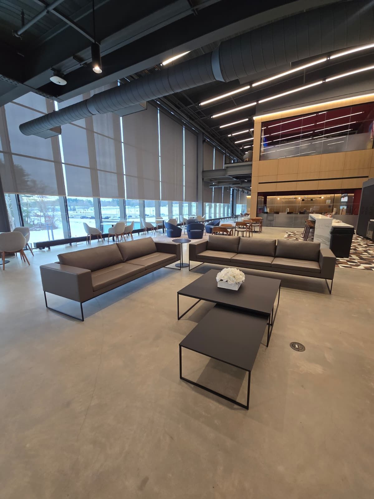 Modern lounge with gray sofas, tables, and large windows in a spacious indoor lobby