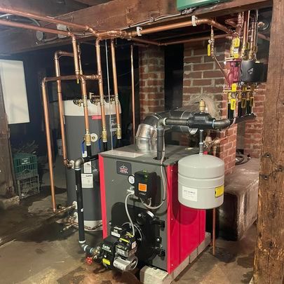 A red and black boiler is sitting in a basement next to a brick wall.