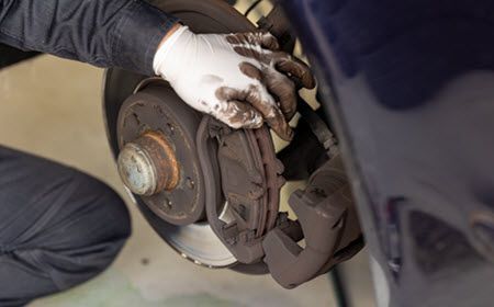 Up close to technician's hand on set of brakes under vehicle | Crowne Automotive