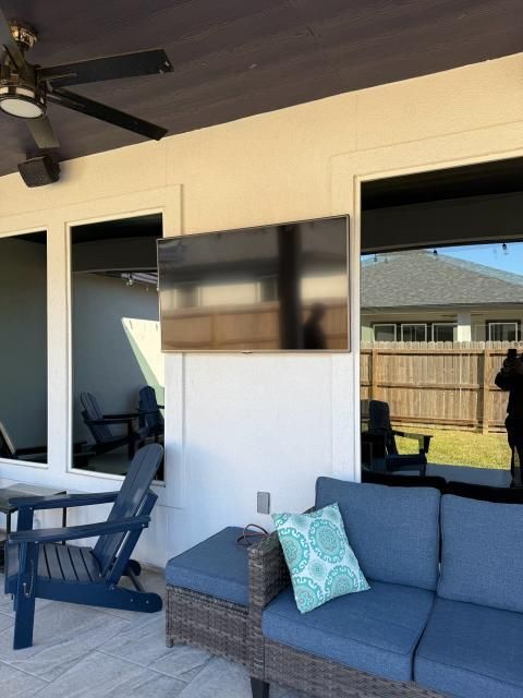 Outdoor patio with a mounted TV, seating area with a blue couch, and a ceiling fan.