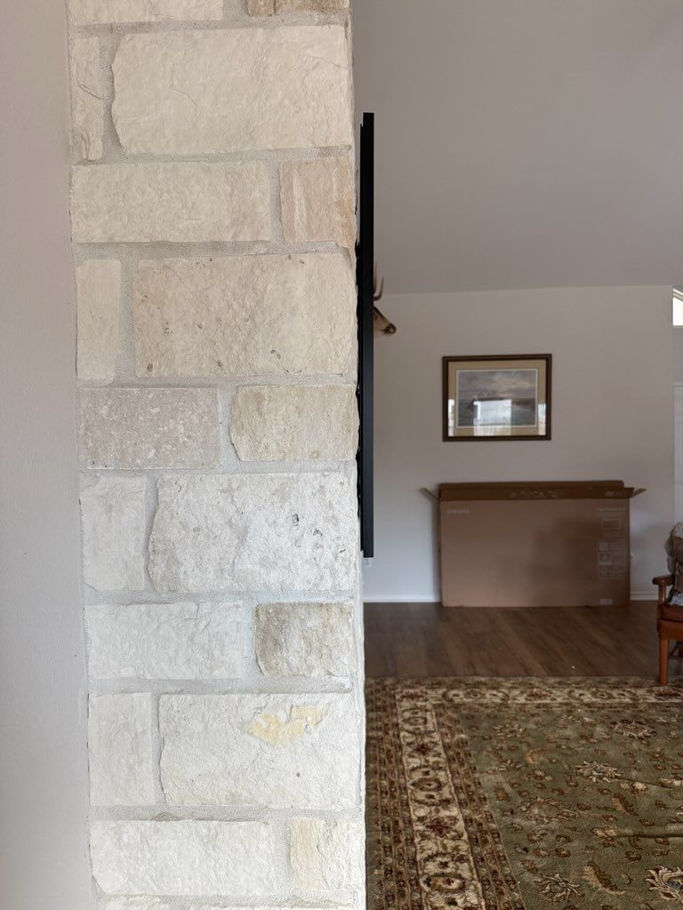 Stone pillar in a room, partially obscuring the view. A brown framed picture and cardboard boxes are visible.