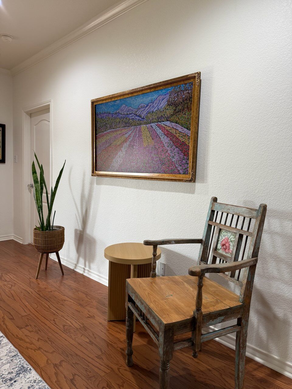 A wooden chair is sitting in a hallway next to a table and a painting on the wall.