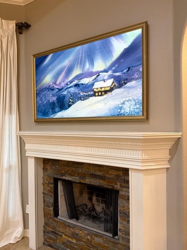 TV displaying winter scene above a fireplace with stone and white mantel. Pale blue and gold tones.