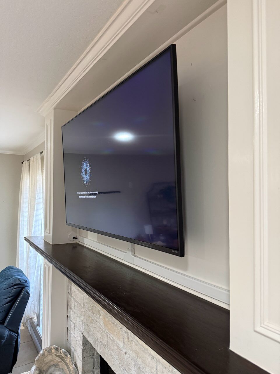 A large, dark television screen mounted on a light-colored wall above a dark wooden fireplace mantel.