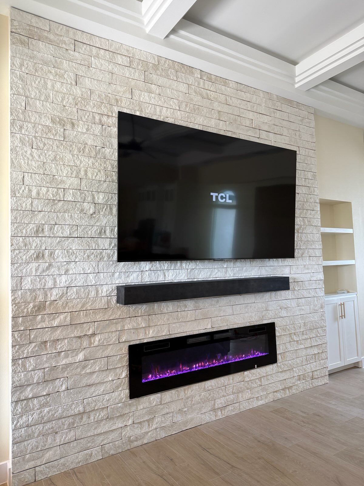 Living room wall with mounted TV above a linear electric fireplace on a white brick accent wall