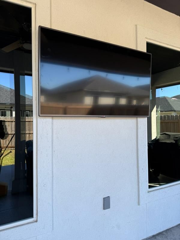 Outdoor TV mounted on a white wall, reflecting surrounding patio and windows.
