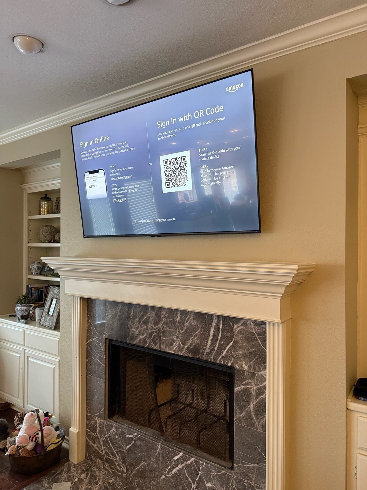 TV mounted above a fireplace, displaying a QR code. Built-in shelves and cabinets are on the left.
