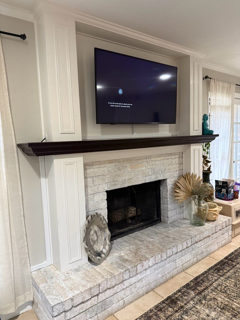 A white brick fireplace with a dark wood mantel and a wall-mounted TV in a neutral-toned living room.