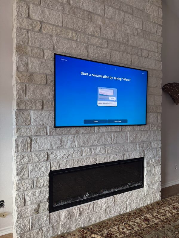 Television displaying a Windows setup screen mounted above a fireplace, both set in a light stone brick wall.